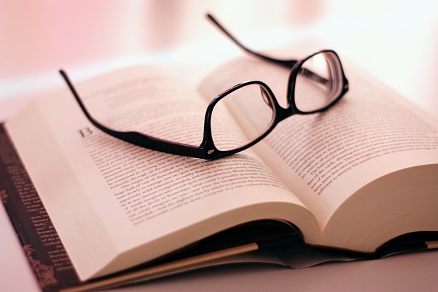 Open book with black reading glasses resting on top. Soft pink background creates a warm, relaxed atmosphere, highlighting themes of reading and knowledge.